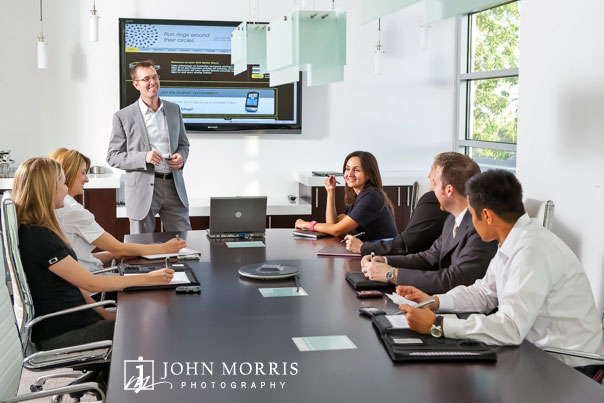 A CEO leads a discussion with a group of executives in a modern conference room during a commercial photo shoot.