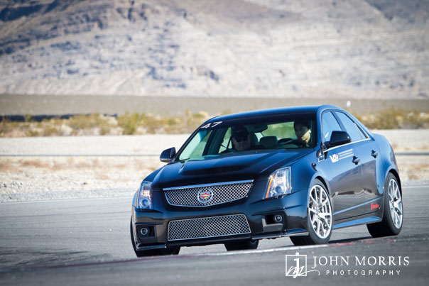 A shiny black Cadillac, being driven on a test drive, exits a tight corner during a commercial shoot in the Nevada desert.