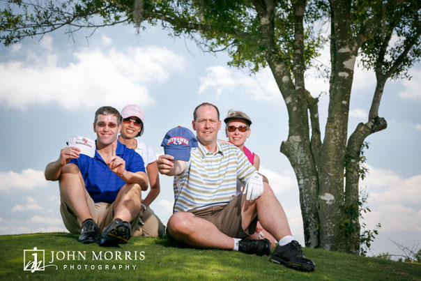 Four golfers seated under and tree and posing for the camera during a corporate golf outing.