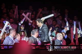 An executive celebrates amongst a crowd of attendees as he makes his way towards the stage during a corporate event.