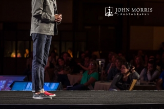 Focus is on the mismatching sneakers worn by an Executive speaker during a conference keynote.