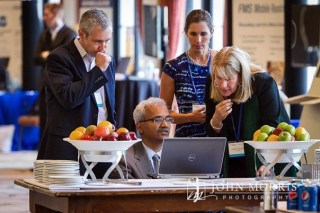 Four conference attendees eagerly huddled around a laptop sharing ideas during a networking event