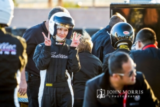 A female driver, wearing full racing gear and helmet gives the thumbs up during a commercial photo shoot.