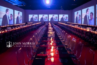 Longs rows of beautiful set tables, surrounded by a dazzling display of big screens, awaits awards winners and attendees before a corporate awards dinner.