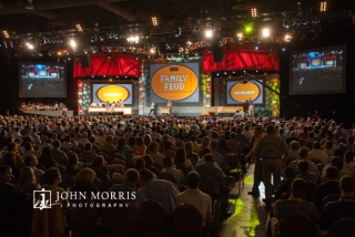 A capacity crowd of attendees pack a convention hall to watch and participate in a mock Family Feud entertainment segment of a corporate event.