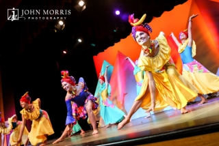 Team of dancers in very colorful costumes, dance with high energy on stage for an audience during a corporate event.