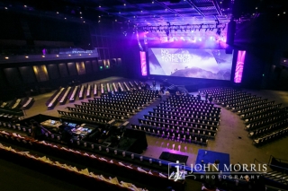 Wide and upper level view of a large arena and stage professionally decorated and prepared by an event company for a corporate event.