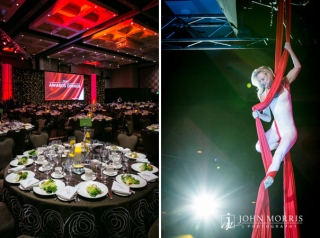 A trapeze artists gracefully hangs from silk material falling from the ceiling during the entertainment portion of a corporate awards dinner.