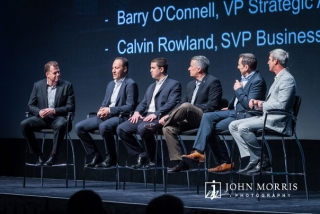 A panel of experts, in professional attire and seated on stage, discussing business topics during a corporate event.