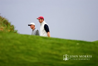 Two golfers, participating in a corporate golf outing, head towards the next green partially hidden by a mound of grass.