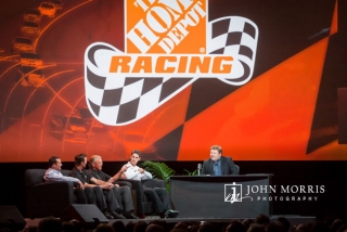 Joe Gibbs and Joey Logano join Comedian Frank Caliendo on stage during a talk to attendees at a corporate event.