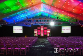 Large, spacious tent and stage are dramatically lit and converted to a conference hall for a corporate event.