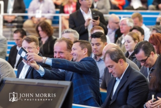 Attendees in business attire, taking a selfie while seated in the audience before the keynote speech at a corporate event.