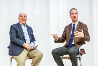 Peyton Manning, seated on stage and sharing a laugh during a question and answer session at a corporate keynote event.