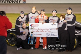 Winning team with a big check in front of a stock car at the Las Vegas Motor Speedway.
