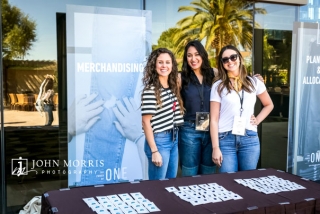 Group of three women manning a booth and smiling for the camera during a outdoor tradeshow event.