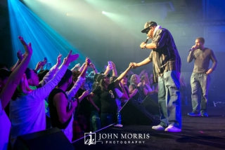 Concerts goers, bathed in blue stage light, reaching out to Ton Loc as he performs on stage.