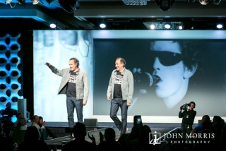 Company executive on stage with his twin in a light hearted moment during a conference keynote.