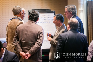 Group of thoughtful attendees gathered around a whiteboard sharing ideas during a breakout session