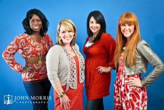 Four members of a women's gospel group smile and pose for the camera in front of a blue background for a publicity photo.
