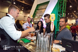Trade show attendees eagerly wait for the bartender to serve up some beer at an exhibit booth.